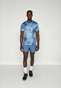 T-shirt de sport en tie-dye bleu, associé à un short bleu uni, des chaussettes blanches et des baskets noires. Présente un petit logo sur le t-shirt.