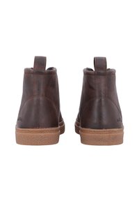 Braune Lederstiefel bis zum Knöchel mit einer strukturierten Oberfläche, sandfarbene Gummisohlen und Zuglaschen an der Rückseite. Genähte Details entlang der Kanten.