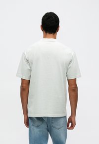 Ανοιχτό γκρι βαμβακερό μπλουζάκι με κοντά μανίκια, στρογγυλή λαιμόκοψη και άνετη γραμμή. Λείο ύφασμα χωρίς ορατά σχέδια ή διακοσμητικά στοιχεία.