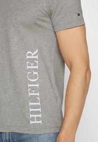 Graues Baumwoll-T-Shirt mit kurzen Ärmeln, mit großem weißen "HILFIGER"-Schriftzug an der Seite. Einfaches, sauberes Design mit Rundhalsausschnitt.