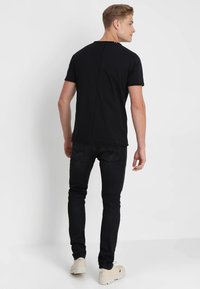 Mustan lyhythihaisen t-paidan suora leikkaus, yhdistettynä slim fit -mustiin farkkuihin ja vaaleisiin kenkiin. Yksinkertainen muotoilu, jolla on sileä pinta.