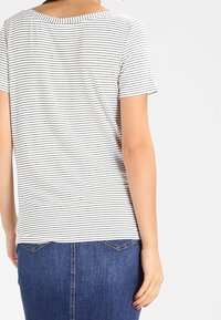 Pasiasta koszulka T-shirt w białym i czarnym kolorze, wykonana z bawełny, z krótkim rękawem i okrągłym dekoltem, zestawiona z dżinsową spódnicą. Gładka faktura.