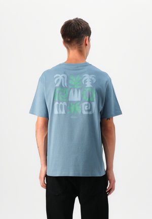 Light blue cotton t-shirt with short sleeves and a graphic design featuring green and gray abstract shapes on the back.