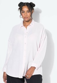 Camicia button-up rosa chiaro in tessuto stropicciato, con colletto e maniche lunghe e morbide. Bottoni argentati completano la texture delicata.