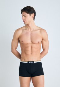 Black boxer briefs with a white and gold waistband, featuring a logo. The fabric appears smooth and soft, fitted to the body.