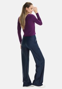Long-sleeve purple top paired with wide-leg navy pants, made from a smooth fabric with a subtle sheen. Features a fitted waist and a clean silhouette.
