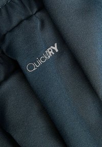 Gros plan sur un tissu texturé bleu foncé avec le mot « QuickDRY » imprimé en blanc sur une section pliée.