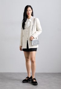 Biały dwurzędowy płaszcz z mieszanki wełny, na biały bluzce z kokardą, w połączeniu z czarną plisowaną spódnicą i masywnymi czarnymi butami na platformie. Srebrna torba na ramię.