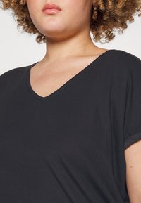T-shirt nera con scollo a V e maniche corte, realizzata in un tessuto morbido. La vista ravvicinata mostra la texture uniforme e la vestibilità rilassata attorno al collo.