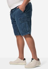 Denimcargo shorts i en mörkblå nyans med sidofickor, dragsko i midjan och en avslappnad passform. Kombinerat med ljusa sneakers.