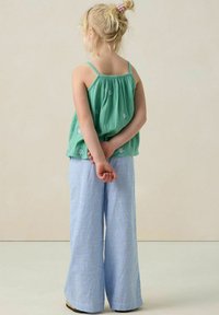 Haut vert sans manches, fluide, orné de broderies en forme de coquillage bleu clair, associé à un pantalon en coton rayé bleu et blanc à jambes larges.