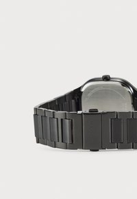 Orologio in metallo nero con cassa rettangolare e design a bracciale collegato. Texture liscia con finitura opaca e lucida. Nome del marchio inciso sulla chiusura.