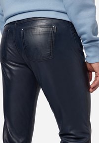 Marine leren broek met twee achterzakken, zichtbare stiksels en een gladde textuur. Beschikt over een getailleerd ontwerp en een subtiele merklabel.