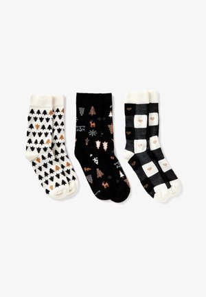 Tres pares de calcetines acogedores: blancos con árboles de Navidad en negro y marrón, negros con árboles festivos y ciervos, y de cuadros en blanco y negro con pequeños corazones marrones.