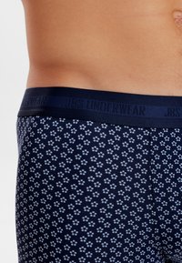 Navy blue boxer briefs with a subtle paw print pattern, featuring a dark waistband printed with "JBS UNDERWEAR" in contrasting lettering.