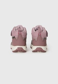 Um par de botas de caminhada para crianças pequenas, cor-de-rosa, com solas brancas, etiquetas Gore-Tex e puxadores em tecido, mostradas pela parte de trás sobre um fundo branco.