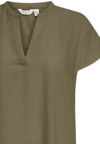 Top de lino verde oliva con escote en V y mangas cortas. La tela tiene un acabado suave y texturizado. Detalles de costura cerca del escote.