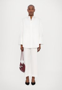 Camicia bianca oversize con bottoni e pantaloni a gamba larga, abbinati a una borsa bordeaux e a delle ballerine nere a punta. Design semplice e pulito.