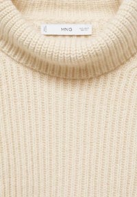 Maglione lavorato a maglia color crema con texture a coste e colletto alto. L'etichetta recita "MNG". Il materiale sembra morbido e caldo.