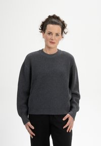Grau gerippter Strickpullover mit rundem Ausschnitt, schmalen Schultern und langen Ärmeln, kombiniert mit dunklen Hosen. Weicher, strukturierter Stoff.