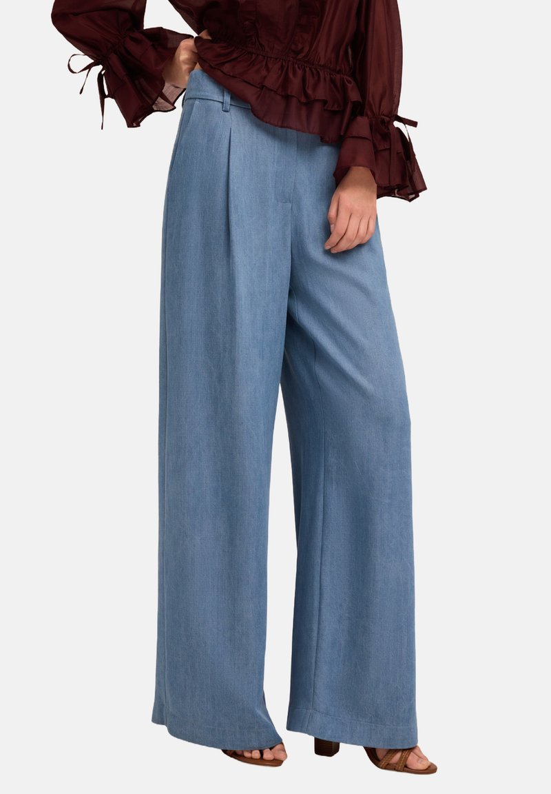 Pantalons large bleu clair en tissu doux et texturé. Présente des plis avant et une taille haute. Associé à un haut bordeaux.