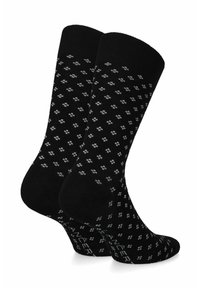 Czarne skarpetki z powtarzającym się małym białym wzorem, z prążkowanym mankietem i wzmocnionym palcem. Na podeszwie znajduje się tekst wskazujący markę lub model.