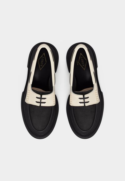 Μαύρα και λευκά δερμάτινα λοφάρια με παχιά σόλα, τρεις οριζόντιες μαύρες ραφές στο επάνω μέρος, απόψη με φόντο γκρι.