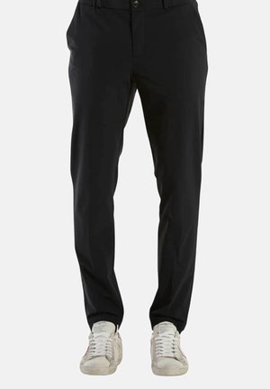 Pantaloni neri in tessuto liscio, con chiusura a bottone e tasche laterali, abbinati a sneakers bianche.