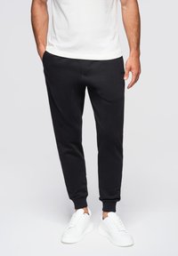 Svarta joggerbyxor med en avsmalnande design, tillverkade av mjukt tyg, med sidofickor och ribbade muddar, kombinerade med vita sneakers.