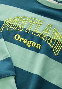 Zelená a tyrkysová proužkovaná mikina s vyšitým nápisem "PORTLAND" v žluté barvě, s kulatým výstřihem a měkkou, texturovanou tkaninou.
