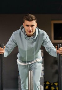 Felpa sportiva azzurro chiaro con joggers coordinati. La felpa presenta un cordino e una tasca; il tessuto appare liscio e aderente.