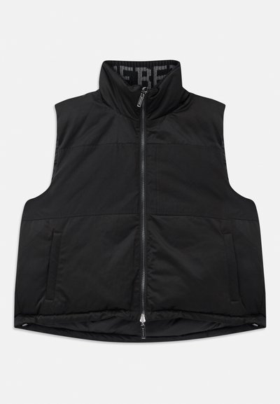 Črna brezrokavnik iz gladkega, podložnega materiala. Ima visok ovratnik, sprednji zadrgo in dva stranska žepa. Notranjost ima vzorčeno podlogo.