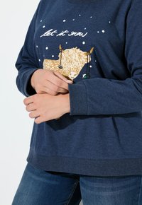 Granatowy sweter z okrągłym dekoltem, zdobiony nadrukiem krowy i płatków śniegu, wykonany z miękkiego materiału z ściągaczami przy mankietach.