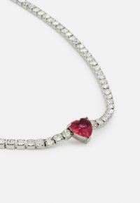 Collier en strass avec un bijou en forme de cœur rouge au centre, doté d'une chaîne en métal argenté et de pierres claires alternées.
