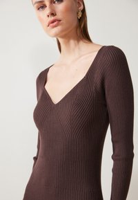 Brown ribbed knit dress with long sleeves and a V-neckline, featuring textured vertical patterns and a fitted silhouette.