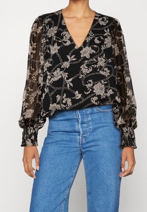 Blusa nera a fiori in tessuto trasparente con scollatura a V profonda, maniche lunghe a sbuffo e polsini elasticizzati, abbinata a jeans blu a vita alta.