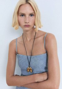 Silver-toned denim dress with spaghetti straps, paired with a black cord necklace featuring a gold, leaf-shaped pendant. Minimalistic design.