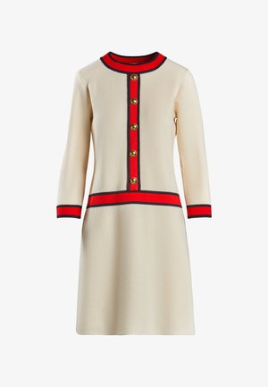 Robe beige jusqu'au genou avec des manches longues, accents rouge et marine, encolure ronde et boutons dorés sur le devant. Texture lisse.