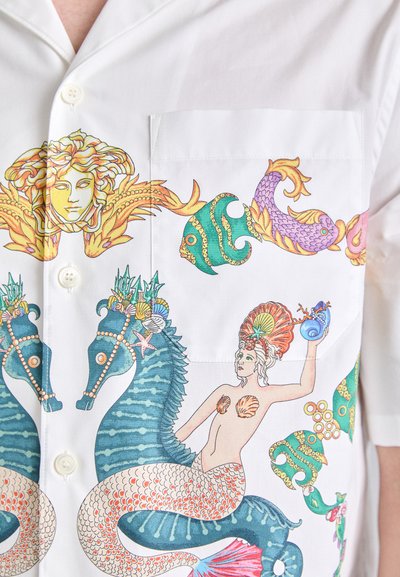 White short-sleeve shirt featuring colorful mermaid and sea-themed illustrations, with detailed motifs of fish, sea horses, and shells.