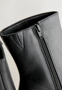 Sorte læder ankelstøvler med en glat overflade, der har en sidezipper og en trekantet udskæring detalje i topkanten.