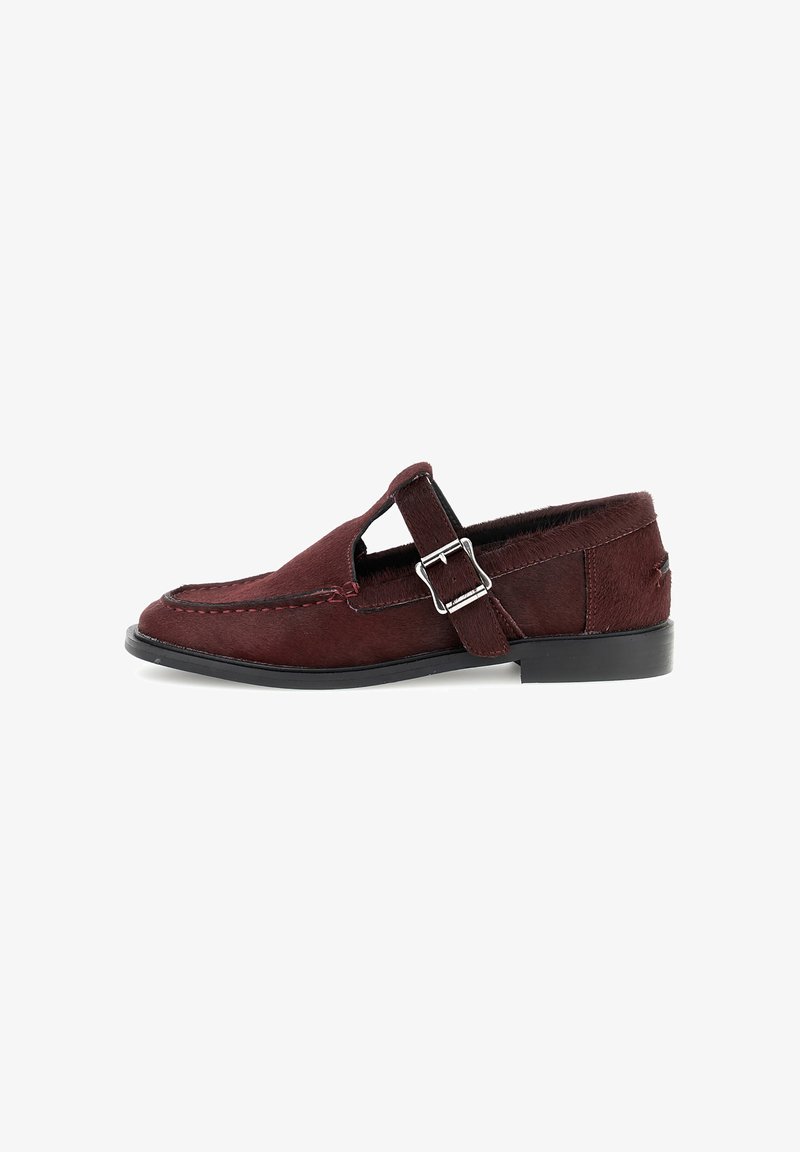 Zapato de piel burdeos con un acabado suave, laterales recortados y un acento de hebilla metálica. Suela baja negra con sutiles detalles de costura.