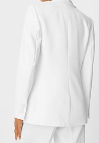 Biały żakiet o dopasowanym kroju, z wyraźnie zarysowanymi ramionami, z jednym rozcięciem z tyłu oraz guzikami na mankietach.