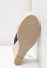 Marinblå kilklack sandal med vävd jute-häl, gummi-sula och strukturerad sula. Etiketten visar "PARFOIS 35" på den beige fotbädden.