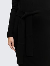 Robe noire avec une texture côtelée et une ceinture en tissu nouée à la taille. Vue rapprochée de la manche et du détail de la ceinture.