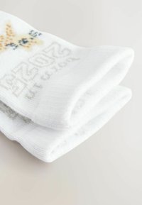 Chaussettes blanches ornées d'un motif de taches orange et noires ressemblant à celles d'une girafe, avec du texte gris clair sur le côté. Tissu doux et texturé.