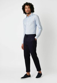 Hellblau kariertes Langarmhemd kombiniert mit navyfarbenen, taillierten Hosen und dunklen Turnschuhen. Baumwollstoff, Knopfleisten-Design und hochgekrempelte Ärmel.