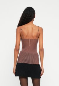 Brun ribbet strikket topp med tynne stropper, tettsittende design og glidelås bak; båret med et svart fluffy miniskjørt.