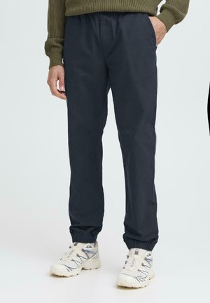 Navy blue athletic pants with an elastic waistband and cuffs. Smooth texture, straight fit, worn with light-colored sneakers.