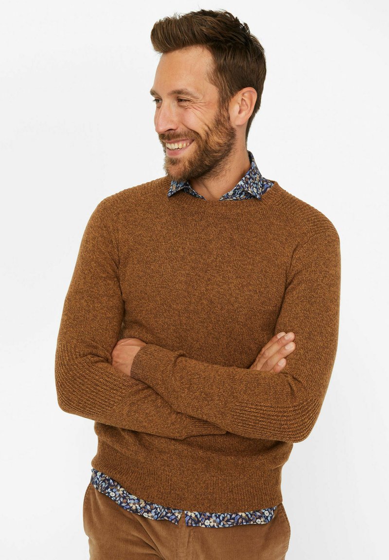 Brauner strukturierter Pullover mit Rundhalsausschnitt, kombiniert mit einem blauen, blumengemusterten Hemd, das darunter hervorschaut.