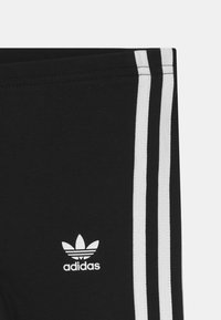Black leggings made of soft fabric featuring three vertical white stripes and a small white Adidas trefoil logo on the left side.